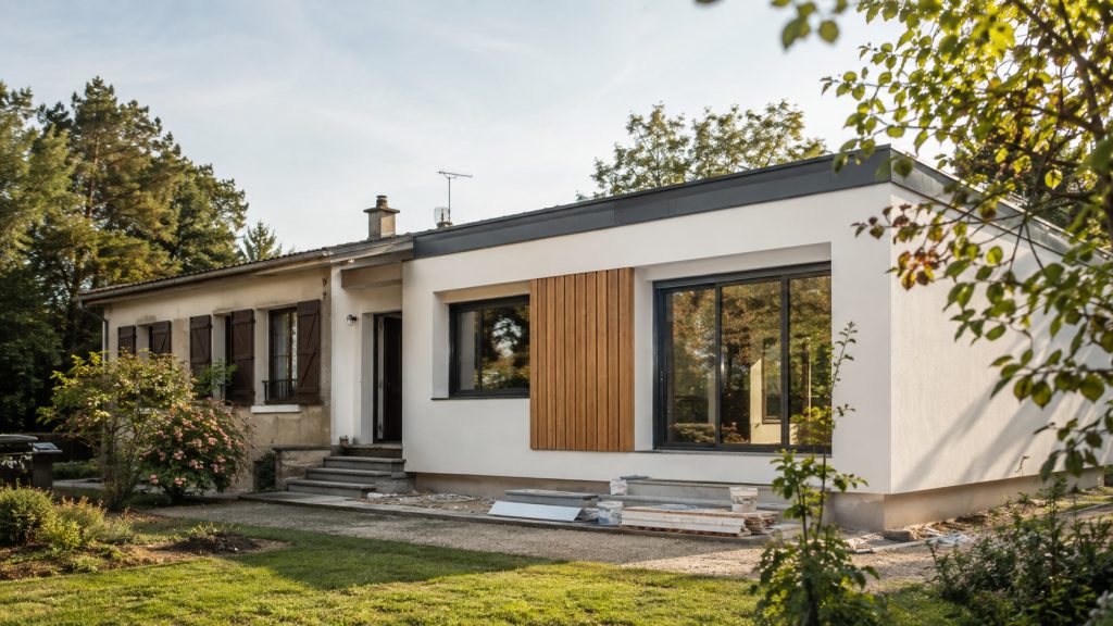 Maison française des années 1970 en cours de rénovation, avec façade d’origine et partie modernisée en enduit clair, bardage bois et menuiseries anthracite.