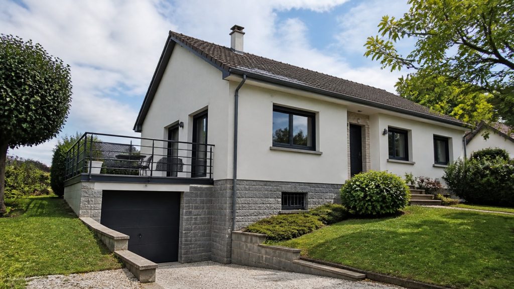 Maison française des années 70 rénovée, construite sur un sous-sol semi-enterré avec garage et terrain en pente.